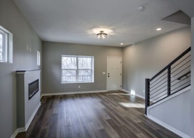 wide space with large windows, custom fireplace, ceiling fan, wooded floor, white ceiling and walls