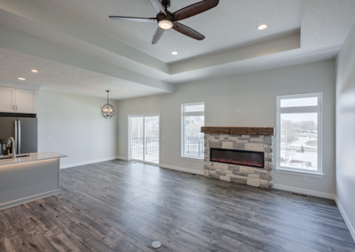 wide space with large windows, custom fireplace, ceiling fan, wooded floor, white ceiling and walls