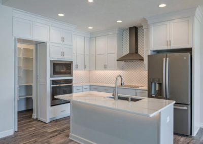 kitchen island with sink, white kitchen cabinets, wooden floor, kitchen lights, double door fridge